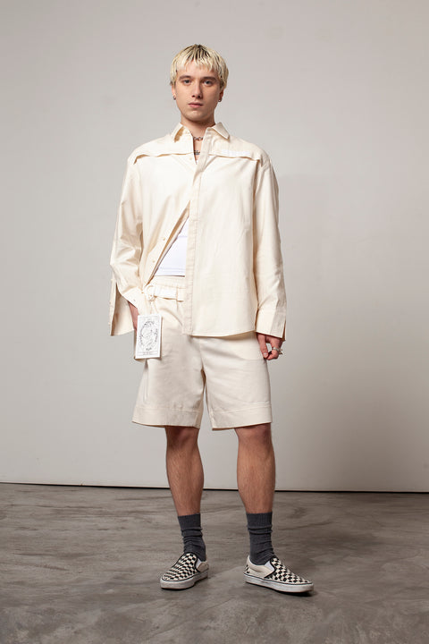 Clément is wearing the White Canvas ESSENTIAL SHORT styled with THE WORLD tag made from leftover deadstock white cotton poplin. The black and white tag has an exclusive design inspired by tarot cards drawn by the artist Maria Robla and is printed in collaboration with RoStudio. Wear the tag alone or attach it to the essential pieces to personalize them. The tag is sold with key holder in recycled plastic made in collaboration with Samji Atelier. White Canvas x Maria Robla.