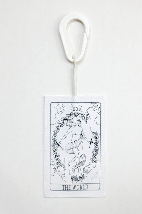 THE WORLD tag is made from leftover deadstock white cotton poplin. The black and white tag has an exclusive design inspired by tarot cards drawn by the artist Maria Robla and is printed in collaboration with RoStudio. Wear the tag alone or attach it to the essential pieces to personalize them. The tag is sold with key holder in recycled plastic made in collaboration with Samji Atelier. White Canvas x Maria Robla.